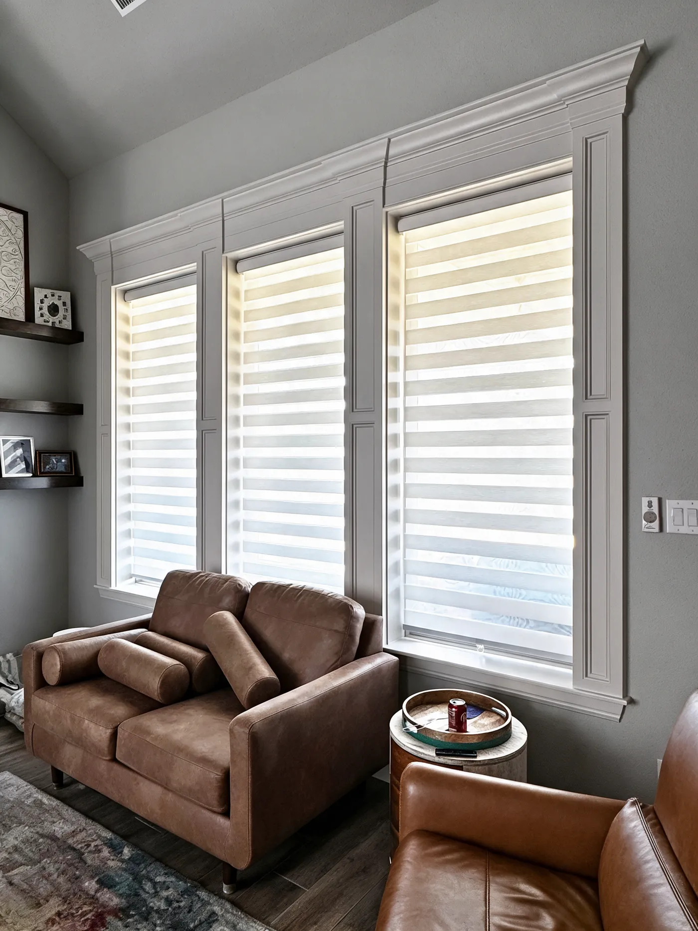Three windows with white zebra shades in a living room with a leather sofa