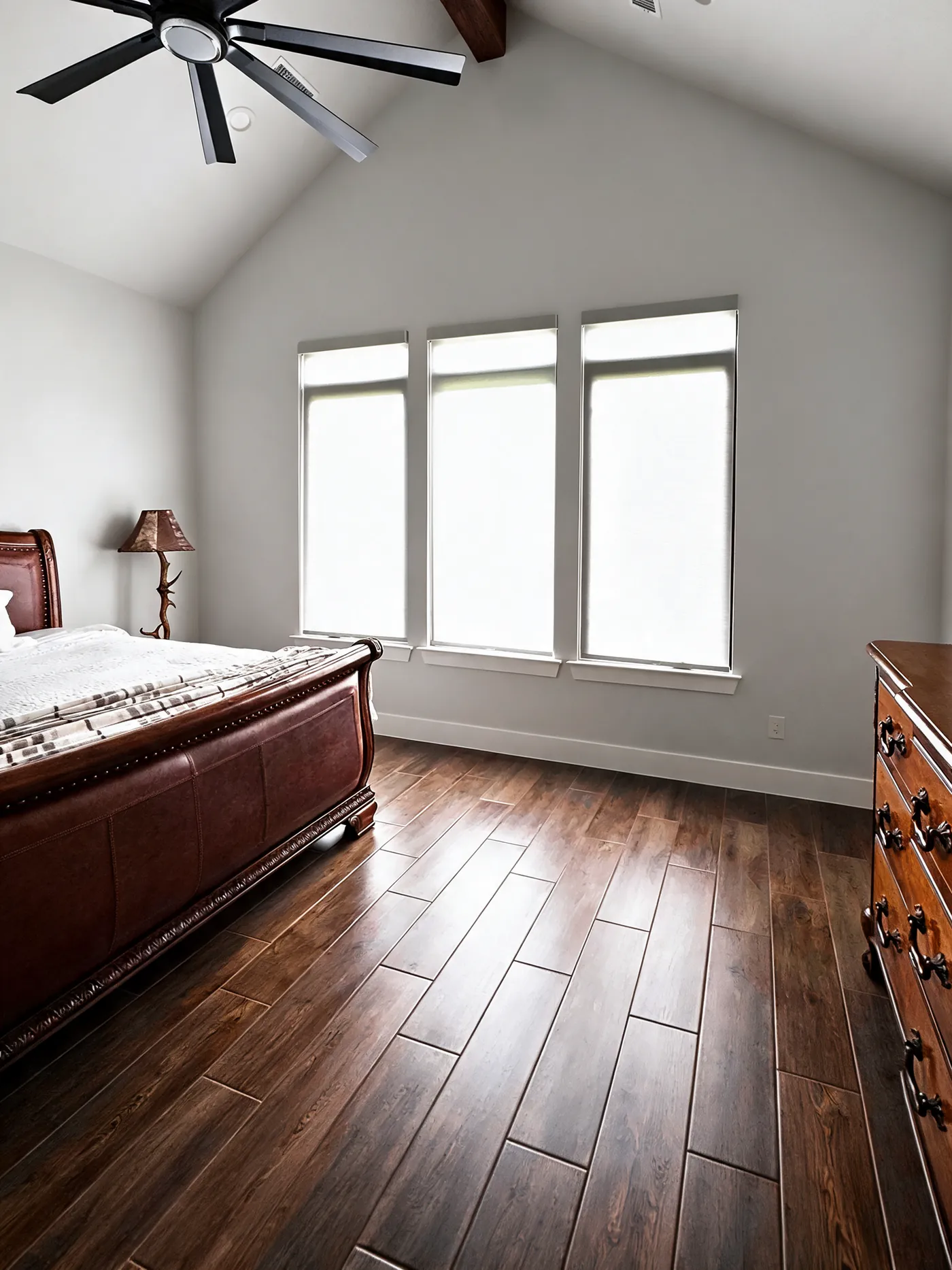 White shades on three windows in a vaulted primary bedroom