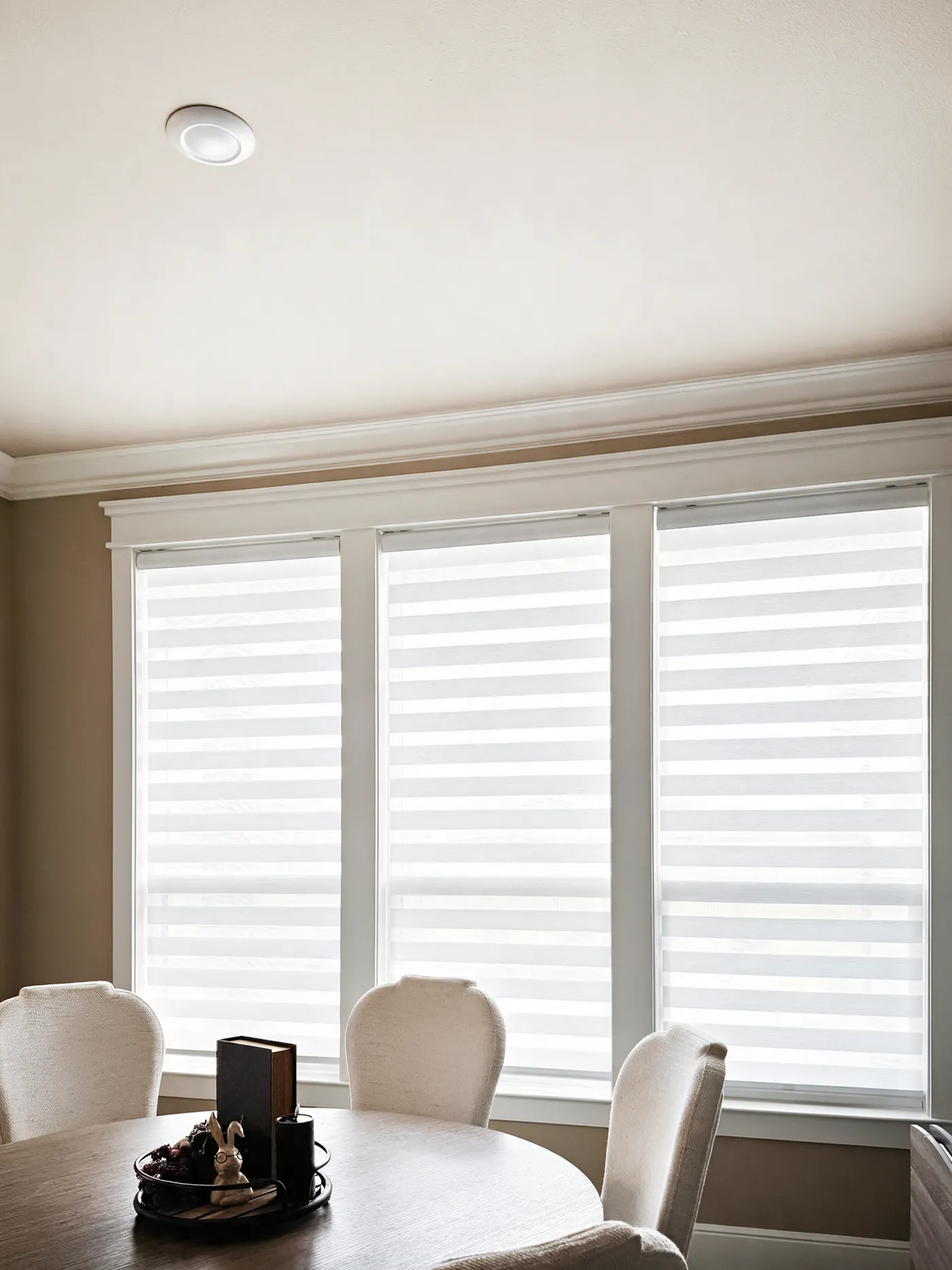Three windows with white zebra shades in a dining area